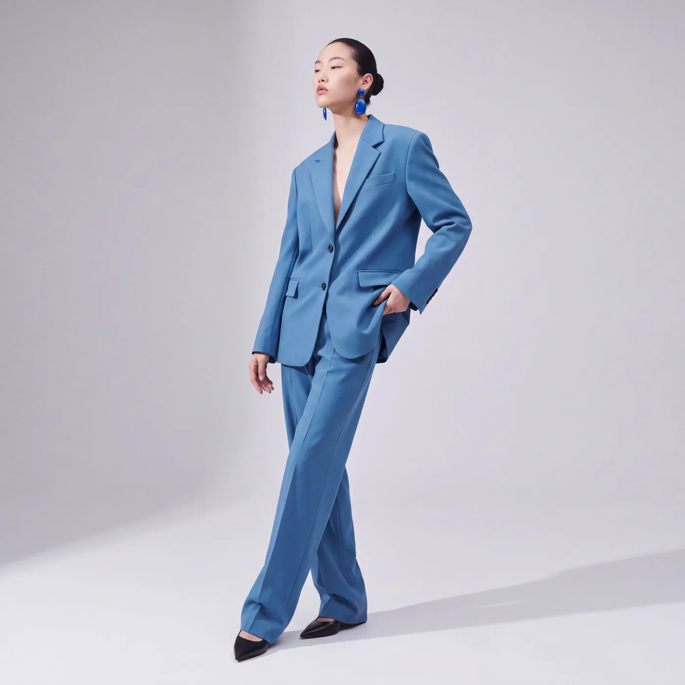 AI-generated on-model shot of a blue oversized suit, hand in pocket, on a light grey studio backdrop
